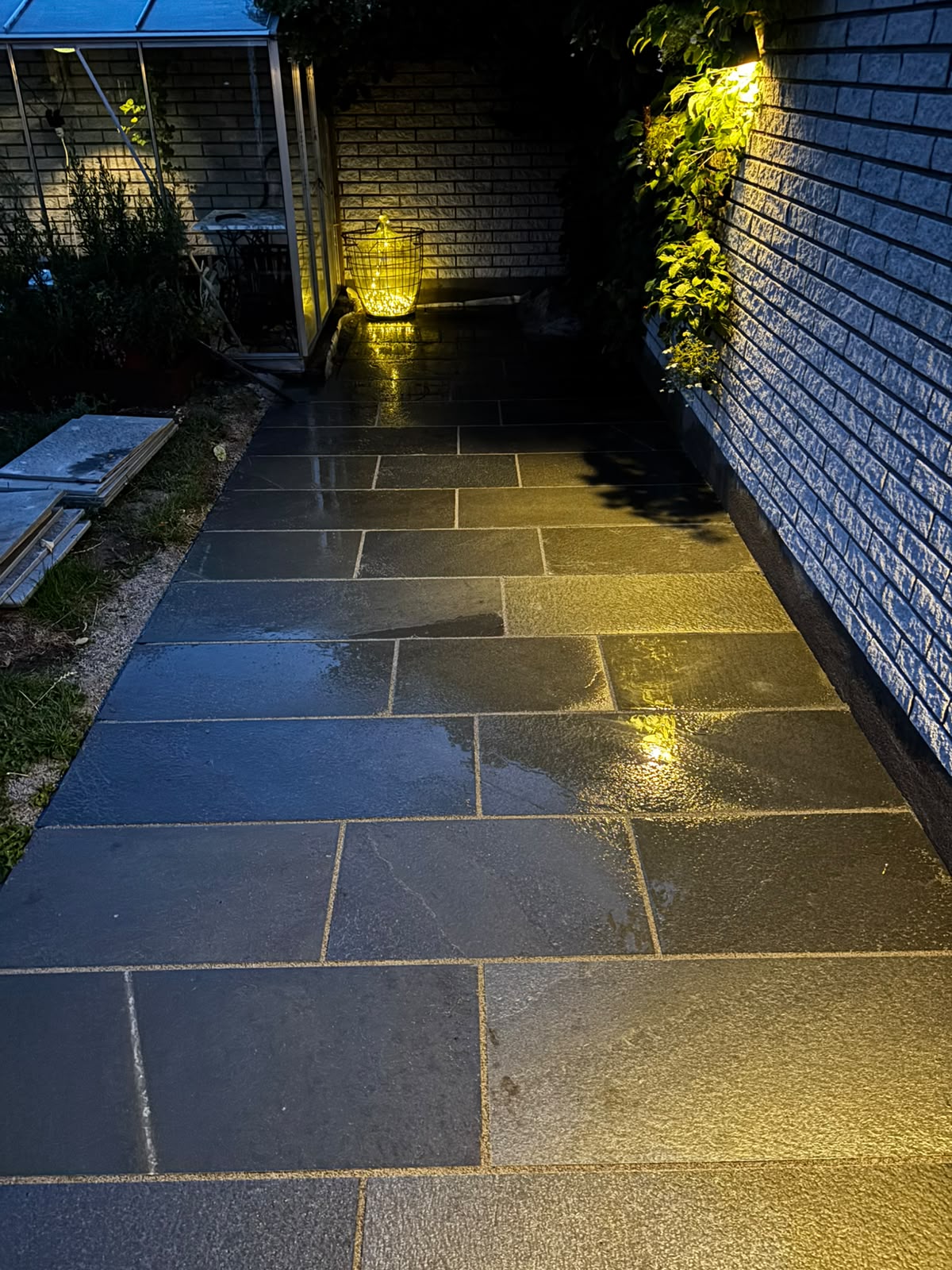 Stone walkway lit by lantern at dusk beside a greenhouse